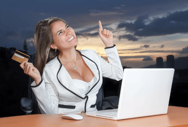 Mujer frente a laptop feliz y con su tarjeta en la mano